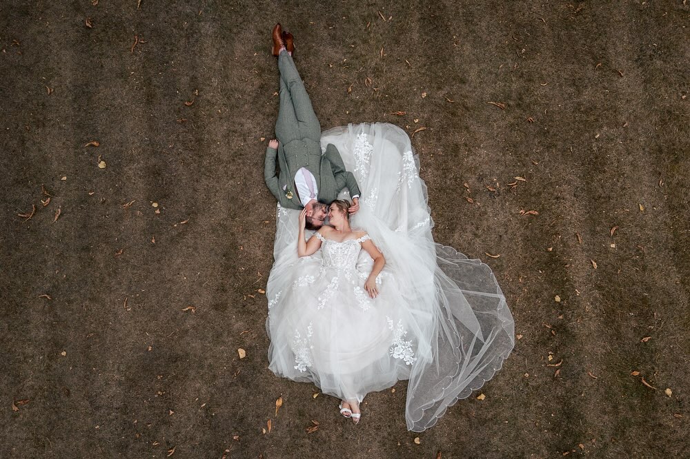 View from above of the bride and groom lay on the grass for a personalised fun wedding