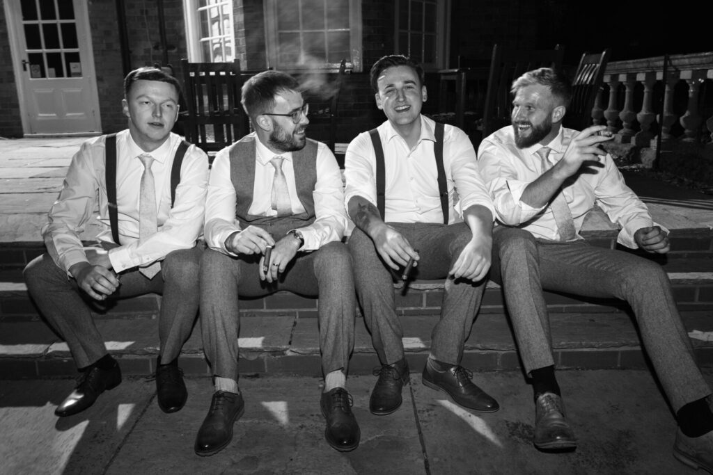 Grooms and groomsmen sat outside smoking cigars for a personalised fun wedding